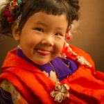 ペロリと舌を出した表情が愛らしい赤い被布と紫の着物を着た3歳女の子