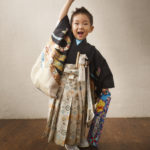 漆喰の壁アンティークフローリングの中元気に手を挙げ笑顔の羽織袴の３歳男の子