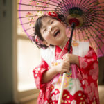 和傘を肩に掛け首を傾げ笑顔の3歳女の子