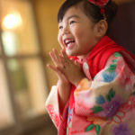 両手を合わせ満面の笑みを浮かべる着物を着た 赤い被布の3歳女の子